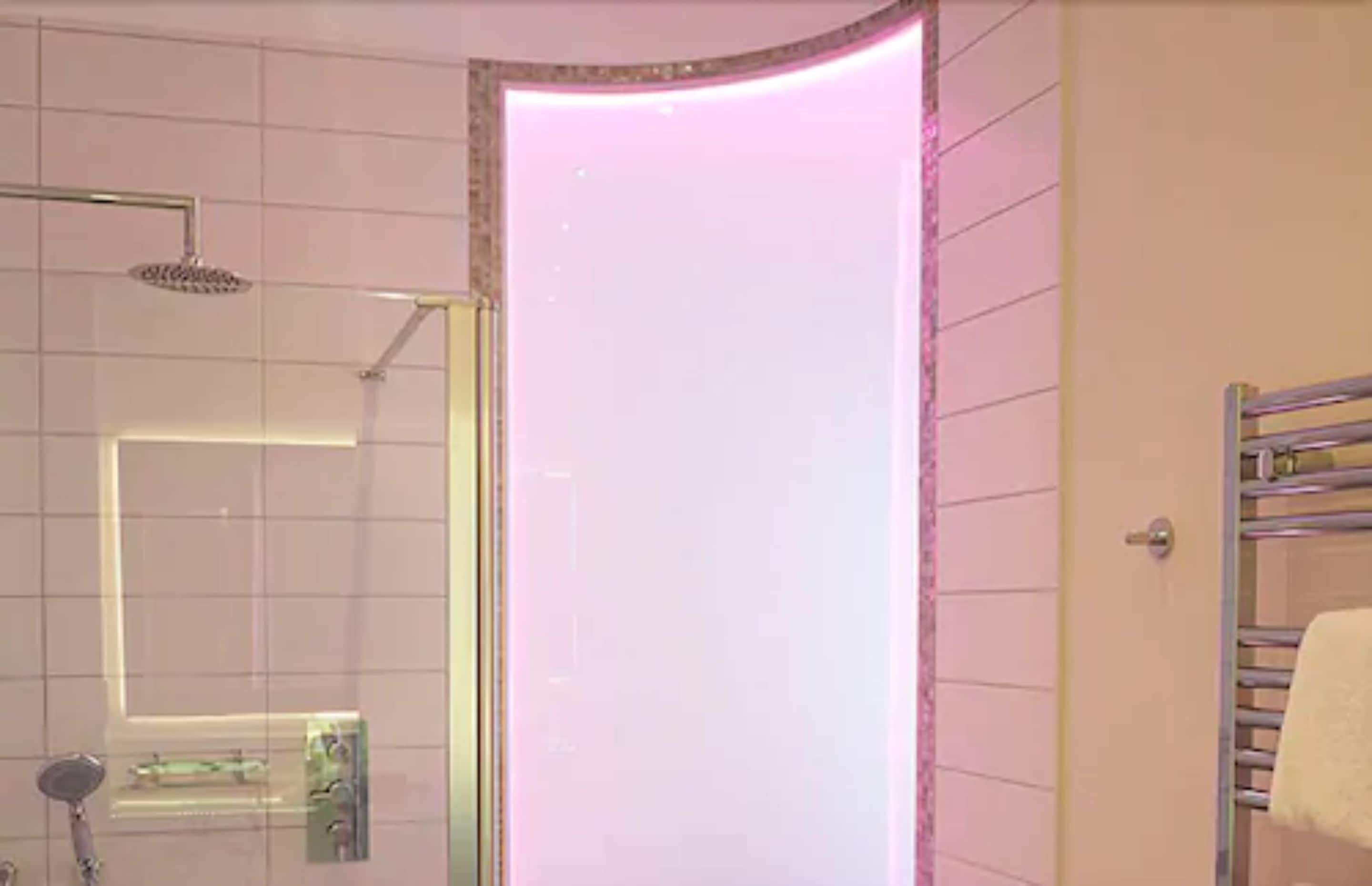 A bathroom with a glass shower enclosure, a visible towel rack, and a door with a pinkish light.