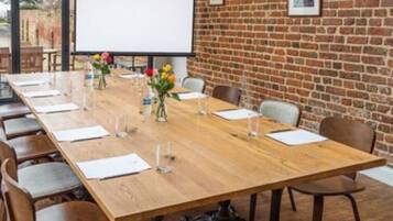 A conference room with a long wooden table, chairs, a projector screen, and a brick wall.