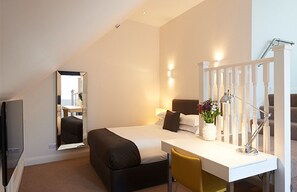 A modern hotel room with a bed, a desk, a chair, a mirror, and a staircase. - The Bell Inn (Stanford-le-Hope)