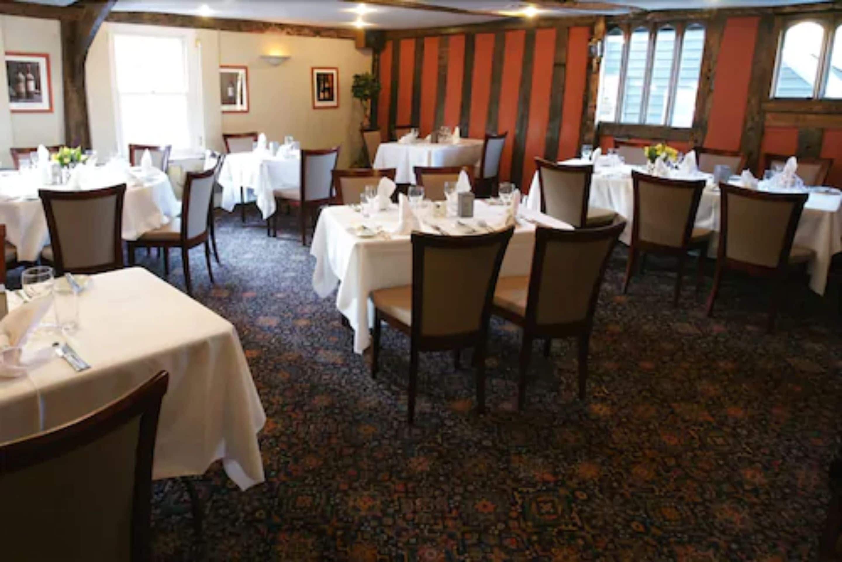 A dining area with round tables and chairs, carpeted floor, and framed pictures on the walls.
