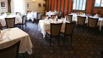 A dining area with round tables and chairs, carpeted floor, and framed pictures on the walls.