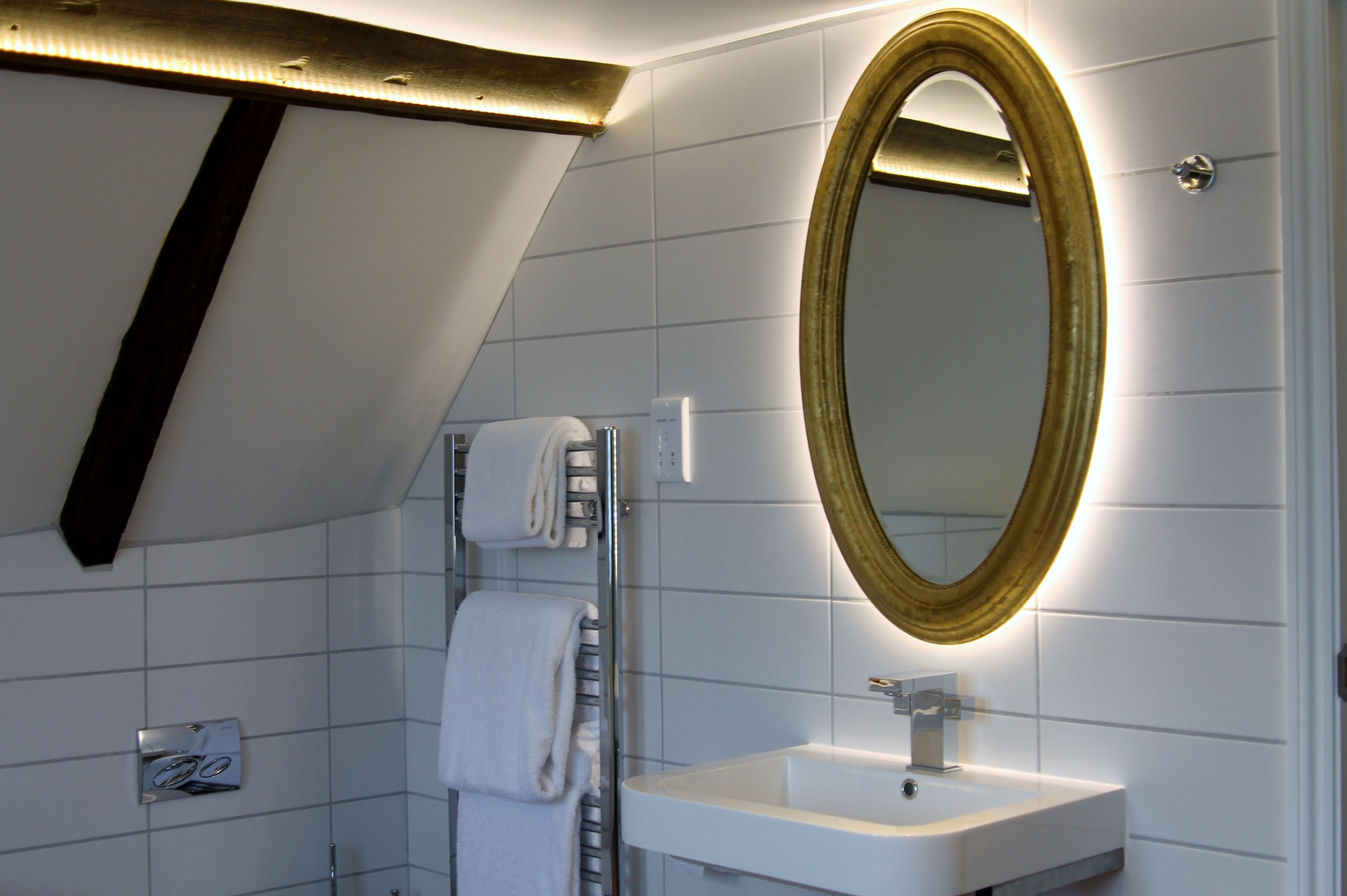 Un baño moderno con un lavamanos blanco, un espejo con marco dorado y un perchero para toallas.