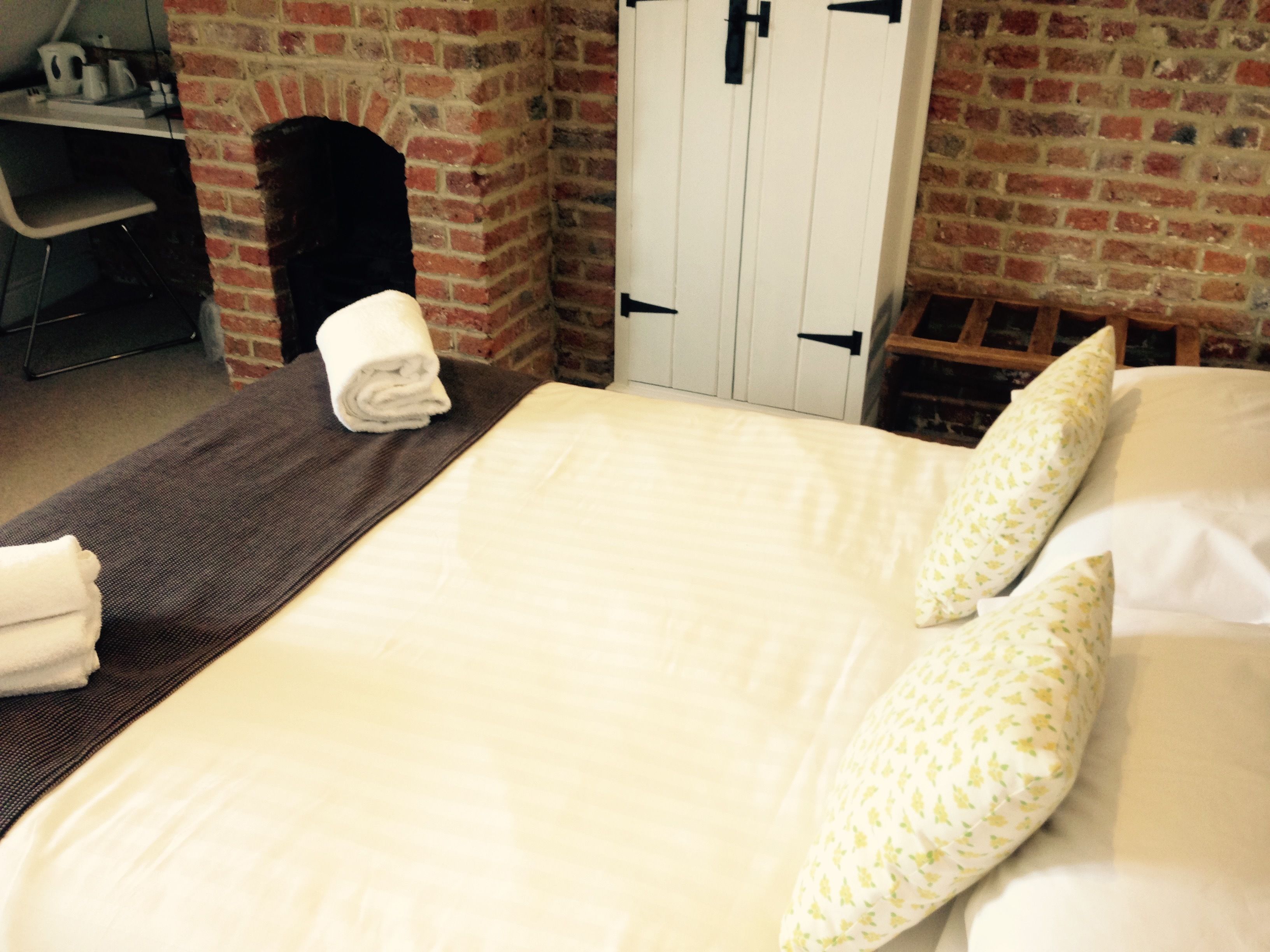 A neatly made bed with white linens and a pillow with a floral pattern. There is a folded towel on the bed and a chair visible in the background.