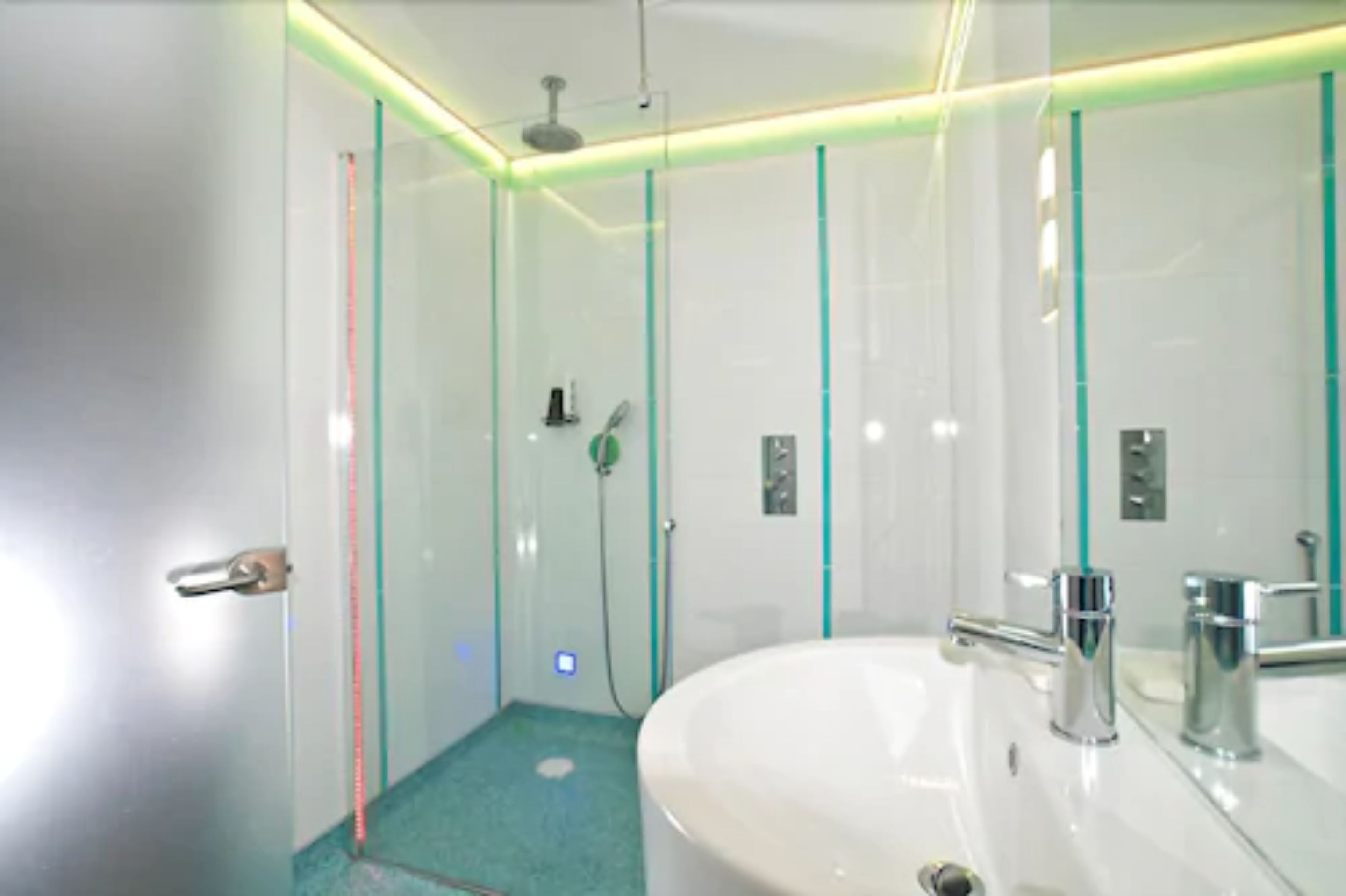 A modern bathroom with a glass shower enclosure, a white sink with chrome fixtures, and teal accents on the walls.