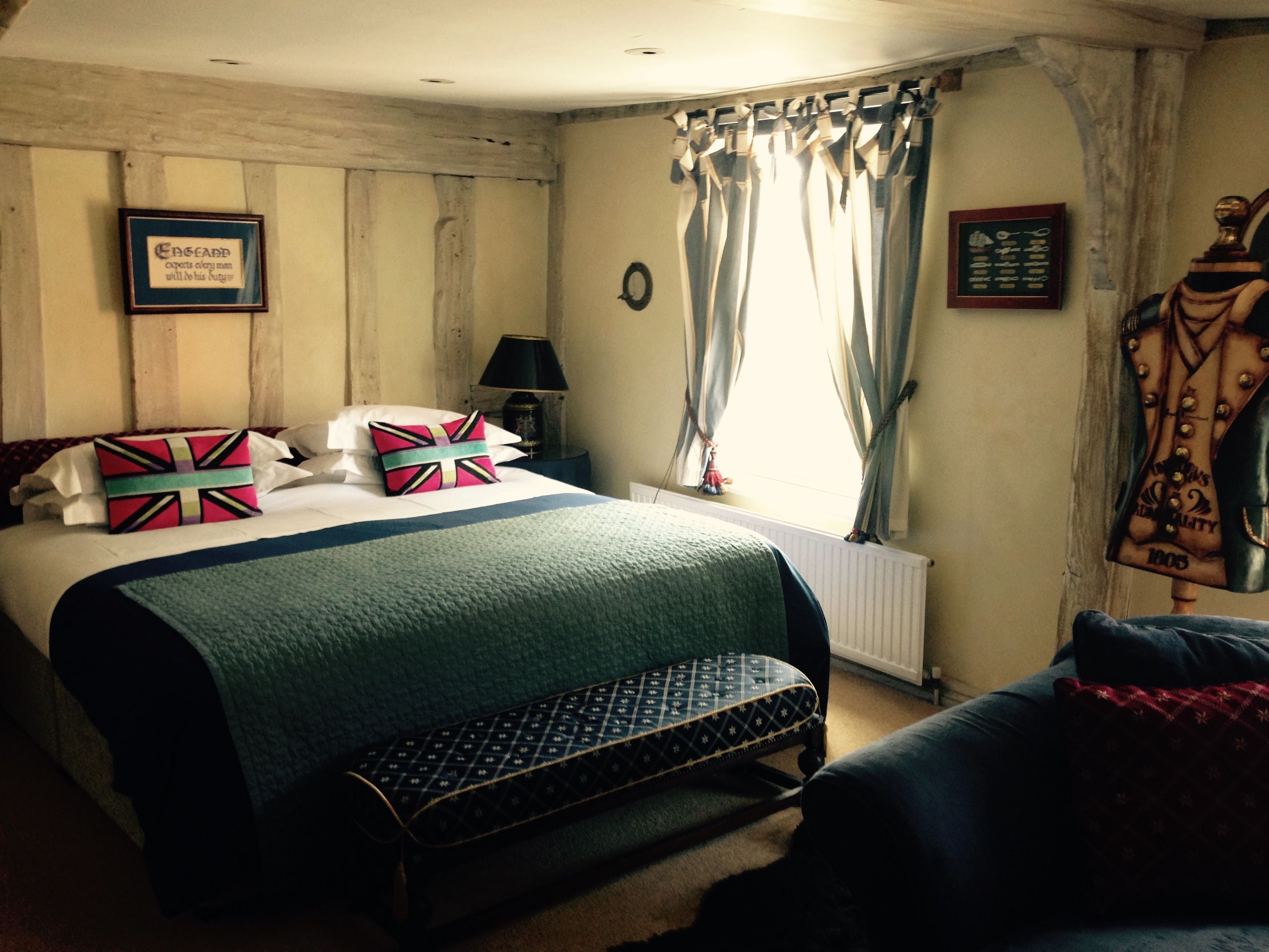 A bedroom with a bed, a bench, a nightstand, a lamp, and a window with curtains.