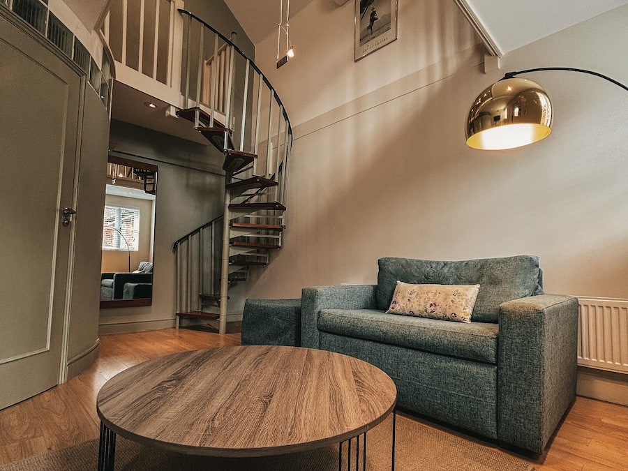 A spacious living area with a wooden coffee table, a blue sofa, and a spiral staircase.