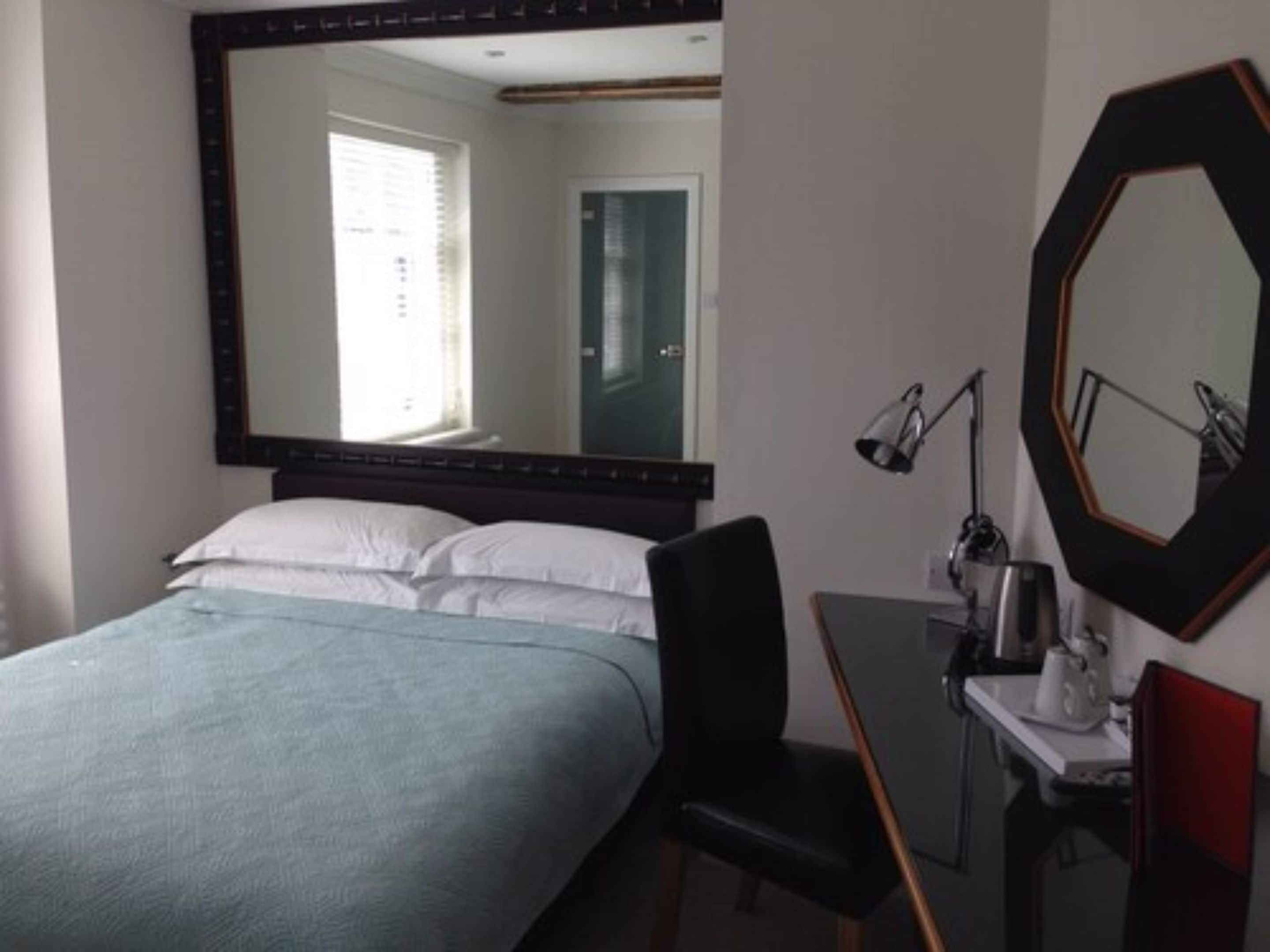Habitación de hotel con cama, escritorio, silla, espejo y ventana.