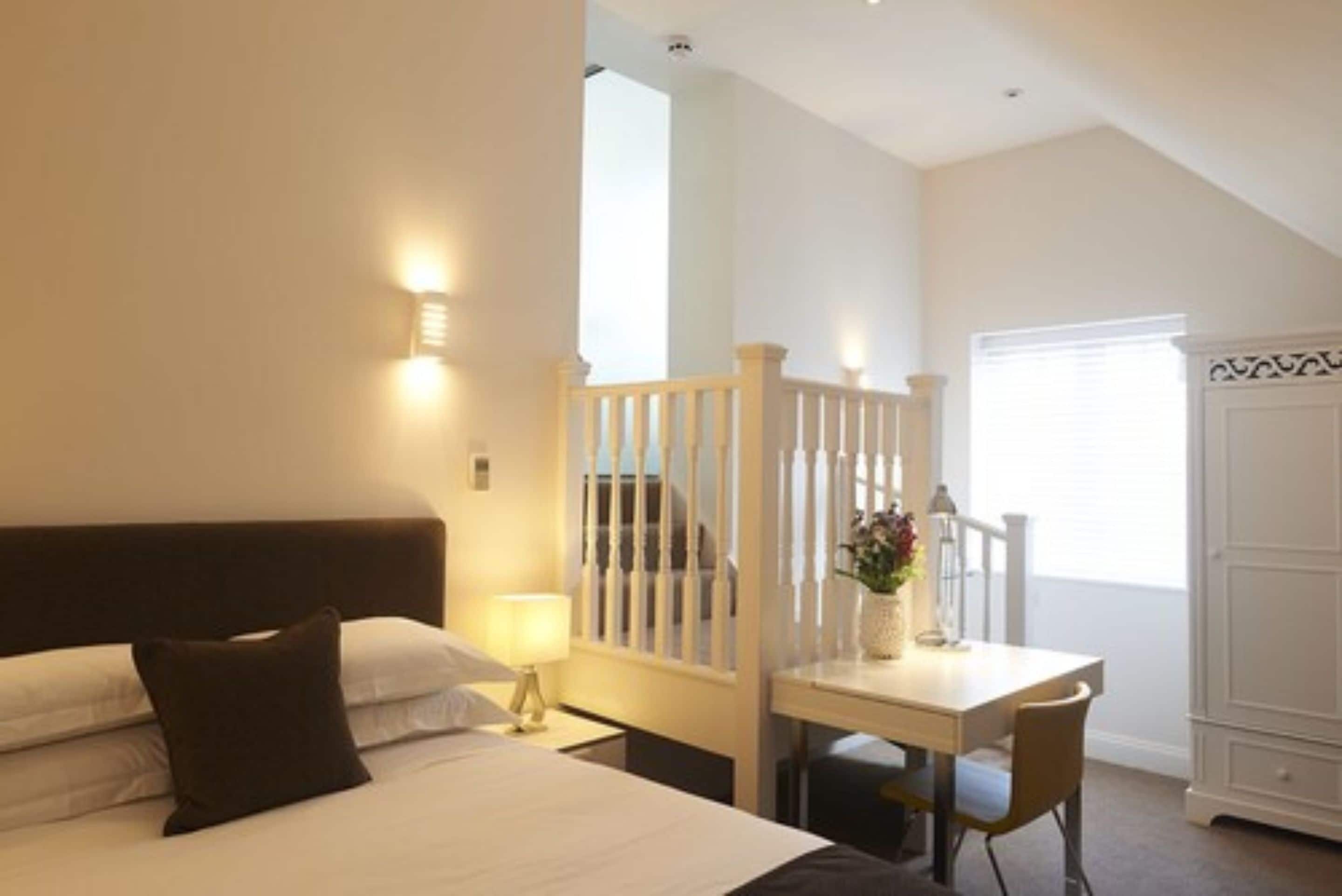 A hotel room with a bed, a desk, and a chair. There is a window with blinds and a door with a decorative panel.