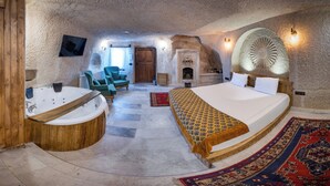Une chambre à coucher avec un grand lit, une baignoire en bois, une cheminée, une télévision et un mur en pierre.