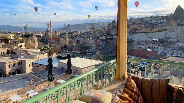 Un balcon offrant une vue sur le paysage urbain, avec des bâtiments et une chaîne de montagnes.