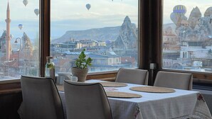 Un coin repas avec une table dressée pour quatre personnes, de grandes fenêtres offrant une vue sur le paysage urbain et des montgolfières.
