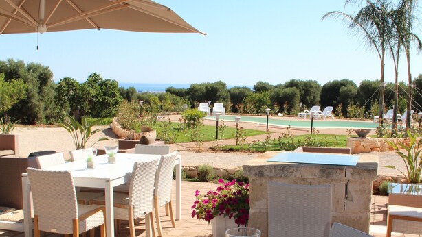An outdoor dining area with tables and chairs, a view of the sea, and a pool in the background. - B&B La Vigna (Carovigno)