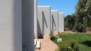 A modern building with white walls and a brick pathway leading to a garden area with flowers and a tree. - B&B La Vigna (Carovigno)