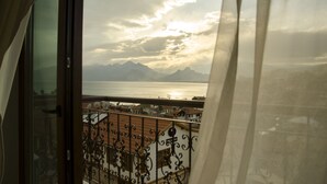 A balcony with wrought iron railings and a view of a body of water with mountains in the distance. - Patron Hotel (Antalya)