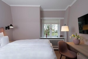 Ein Hotelzimmer mit Bett, Schreibtisch, Stuhl, Fenster mit Aussicht und Lampe.