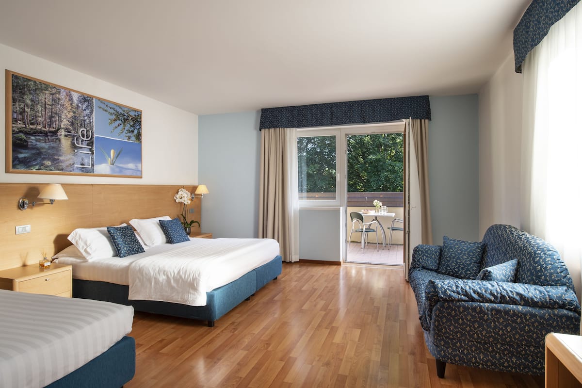 A hotel room with a large bed, a sofa, a dining area with a table and chairs, and a large window with curtains.