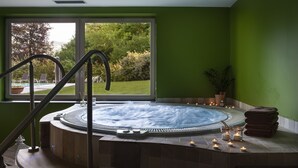 Un jacuzzi con vistas a un jardín y una piscina exteriores, una escalera que lo lleva y velas en el suelo.