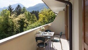 Un balcón con una mesa dispuesta para dos personas, con vistas a una cadena montañosa boscosa.