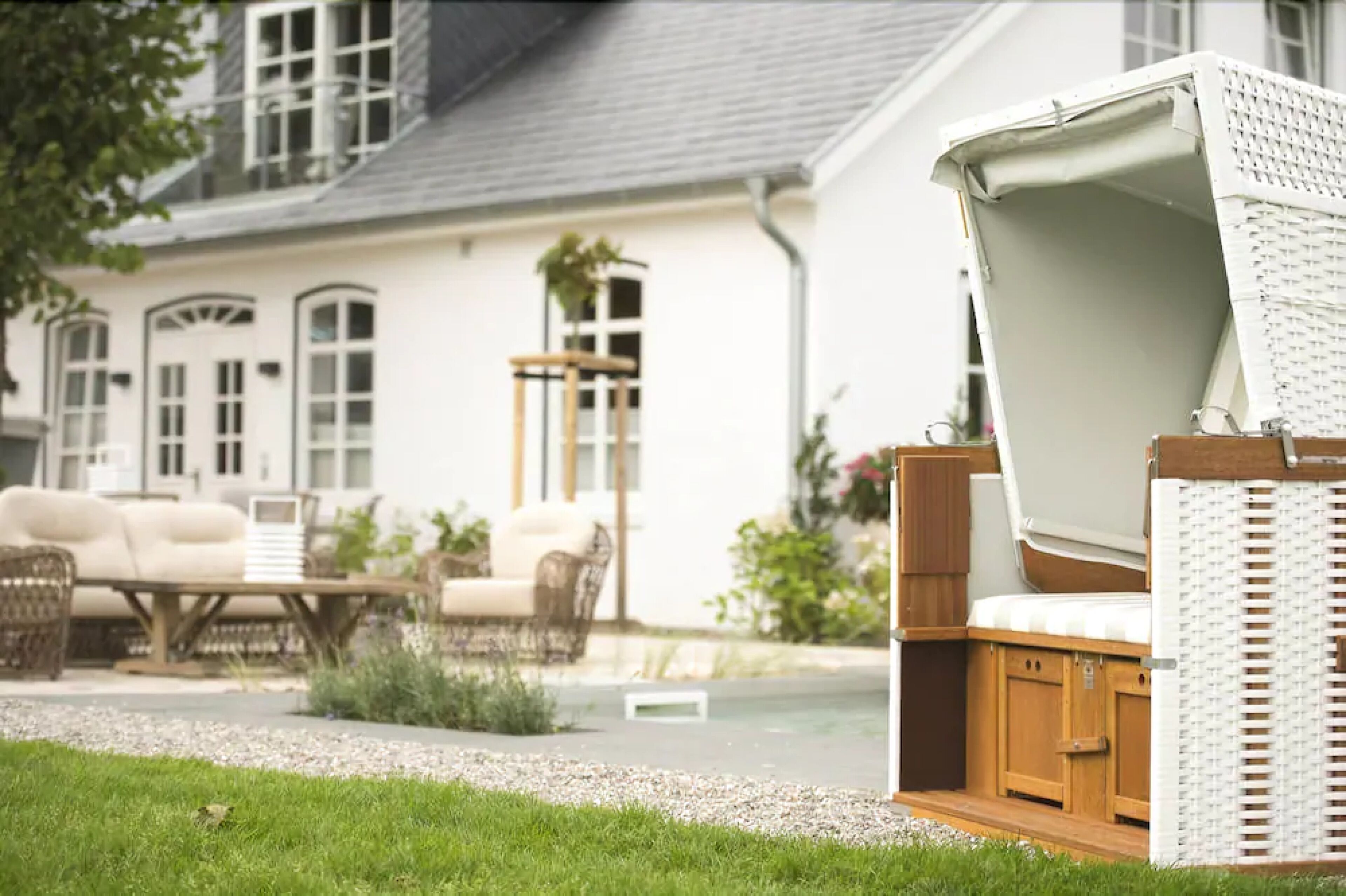 Una casa bianca con una zona salotto esterna coperta, un patio in legno e un giardino.