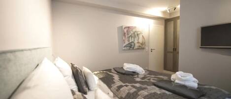 A hotel room with a bed, pillows, a folded towel, a painting on the wall, and a door.