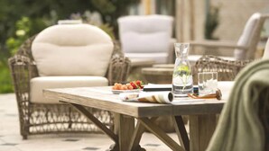 Un espace extérieur aménagé avec des meubles en osier et une table où sont disposés une bouteille, un verre et des fruits.