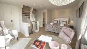 Une chambre à coucher avec un lit, une chaise, une table avec des livres, un escalier et un lustre.