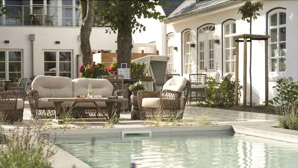 Un espace aménagé au bord de la piscine, avec des meubles en osier, un canapé blanc et une table où sont disposées des boissons.
