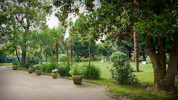 Uma trilha pavimentada bordeada por grandes vasos de plantas e árvores, que conduz a uma área gramada com um gazebo.