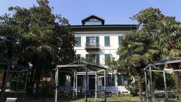 Un edificio grande con balcón, rodeado de palmeras y estructuras cubiertas.