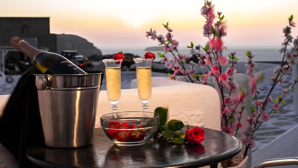 Une table avec une bouteille de champagne, deux coupes de champagne, un saladier de fraises et une rose.