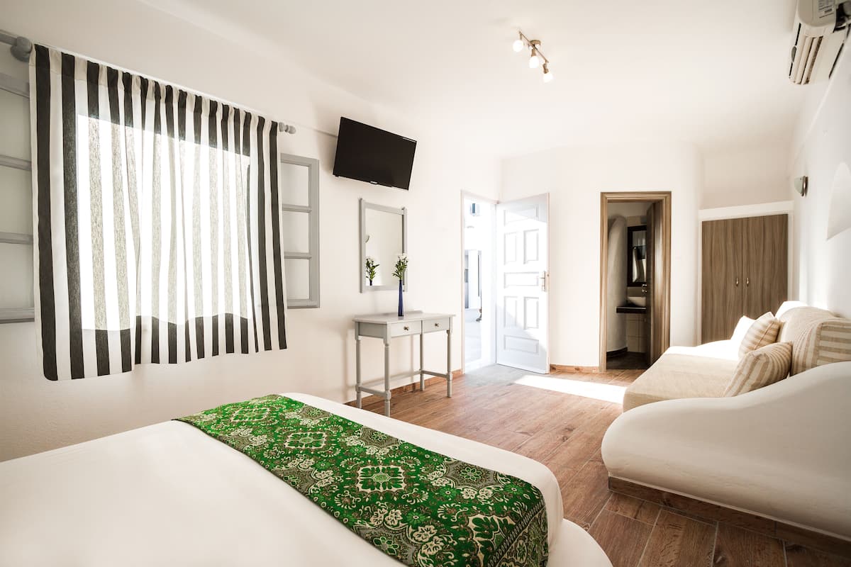 Ein Hotelzimmer mit Bett, Schreibtisch, Fernseher, Kleiderschrank und einem durchgegangene Tür sichtbaren Badezimmer.