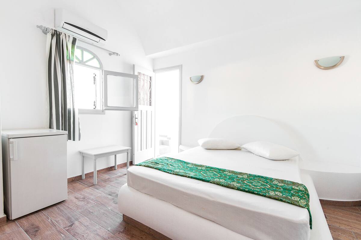 Ein schlicht eingerichtetes Schlafzimmer mit einem Bett, einem kleinen Schreibtisch und einer Wand-Klimaanlage.