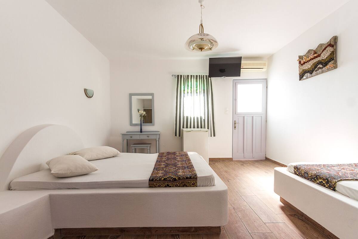 Ein Schlafzimmer mit Bett, Nachttisch, Spiegel, Fernseher und einer Tür.