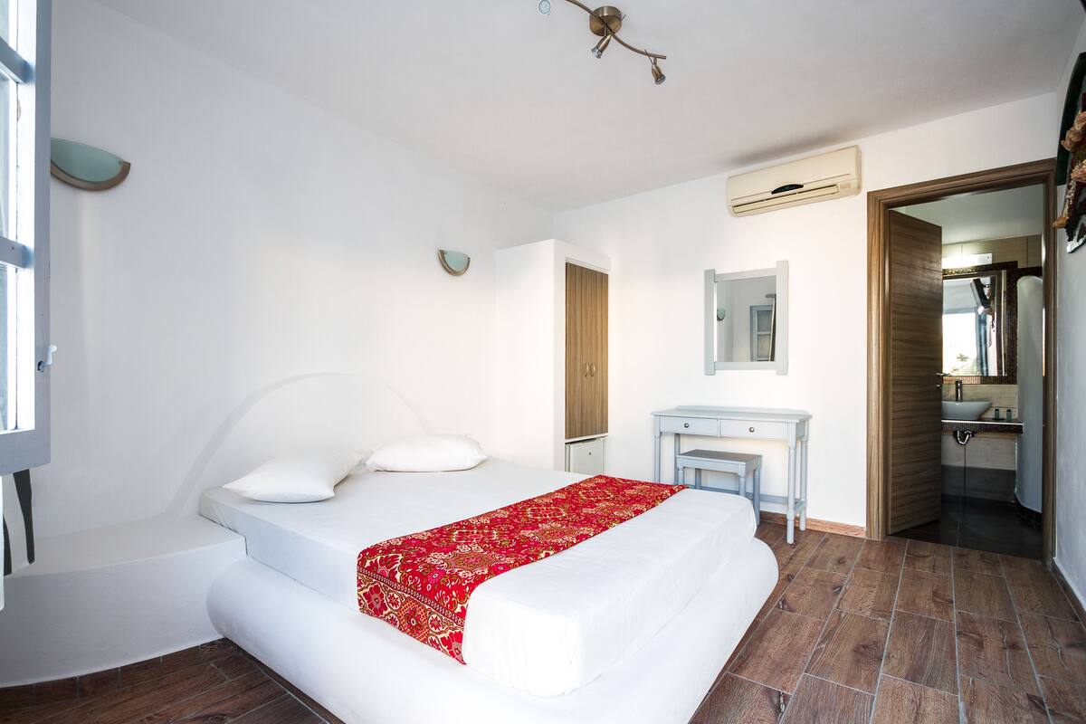 Ein Schlafzimmer mit Bett, Nachttisch, Spiegel und angrenzendem Badezimmer, durch eine offene Tür sichtbar.