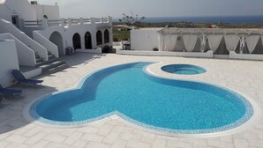 Une piscine sur le toit offrant une vue dégagée sur la mer, entourée de bâtiments blancs dotés d’arcades et d’une terrasse carrelée.