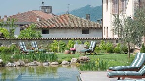 A pool area with lounge chairs, a stone wall, and a view of buildings and mountains. - Boutique Hotel Villa dei Campi (Gavardo)