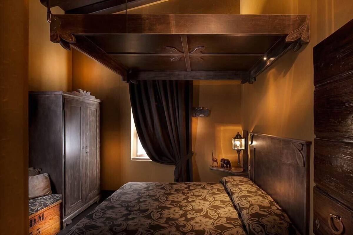 A bedroom with a wooden headboard, a bed with a patterned bedspread, a wardrobe, and a nightstand with a lamp.