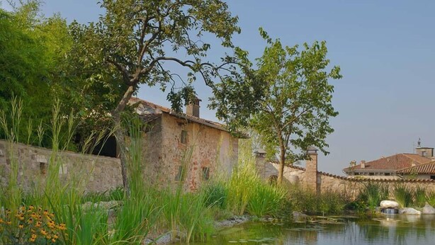 A serene pond with lily pads and a stone wall, surrounded by lush greenery and a rustic building with a tiled roof. - Boutique Hotel Villa dei Campi (Gavardo)
