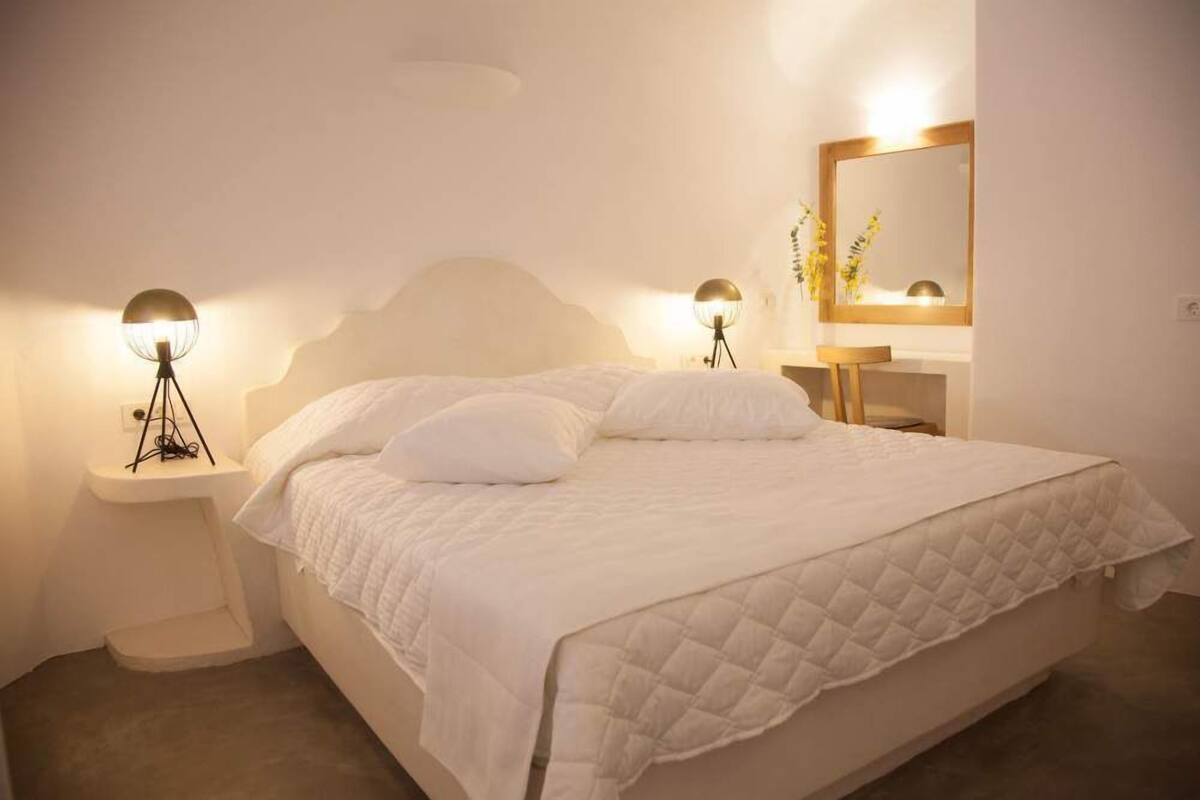 A bedroom with a large bed, bedside lamps, a bedside table, a mirror, and a small plant.