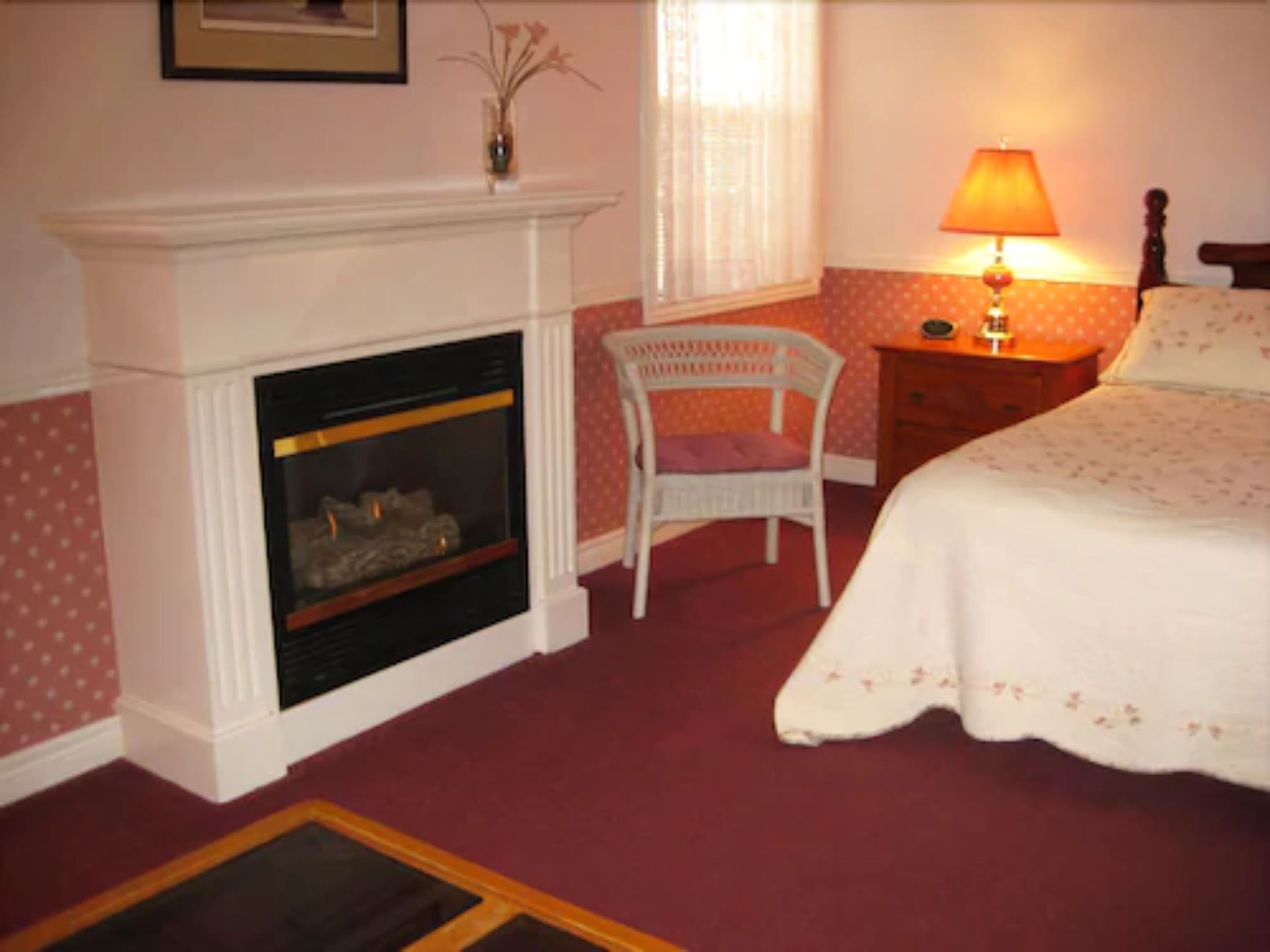 A bedroom with a fireplace, a chair, a bedside table with a lamp, and a bed.