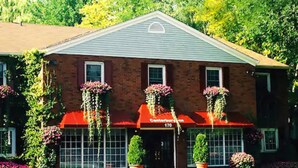 A brick building with a red awning and hanging flower baskets. - Canterbury Inn (Niagara-on-the-Lake)