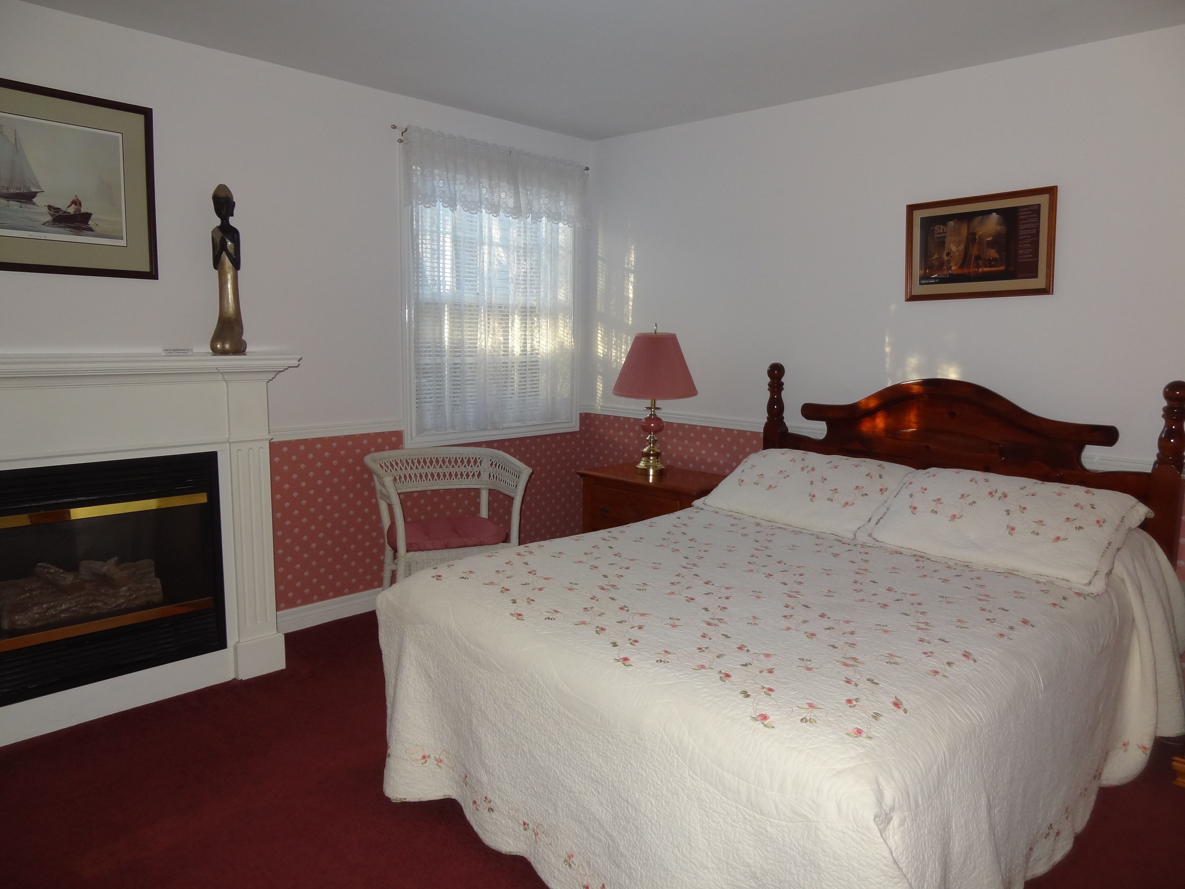 A bedroom with a bed, a chair, a nightstand, a lamp, a fireplace, and a window with curtains.