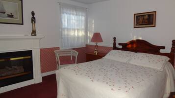 A bedroom with a bed, a chair, a nightstand, a lamp, a fireplace, and a window with curtains.