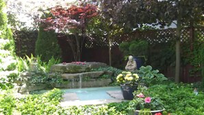 A garden with a small pond, a statue, and various potted plants. - Canterbury Inn (Niagara-on-the-Lake)