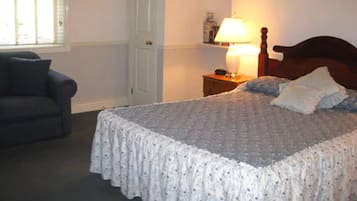 A bedroom with a bed, a nightstand, a lamp, a chair, and a door.