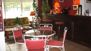A dining area with a round table and four chairs, a sofa, a bar counter, and a window with curtains. - Canterbury Inn (Niagara-on-the-Lake)