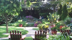 A garden with a pathway, wooden chairs, and potted plants. - Canterbury Inn (Niagara-on-the-Lake)