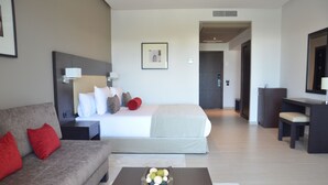 Une chambre d’hôtel moderne équipée d’un lit, d’un canapé, d’une table basse avec des fruits, d’un bureau et d’un miroir.