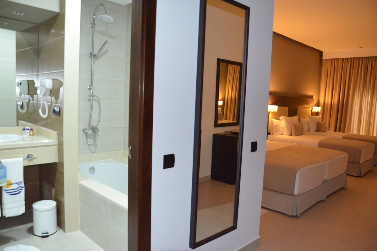 A hotel room with a bathroom, a large mirror, two beds, and a nightstand.