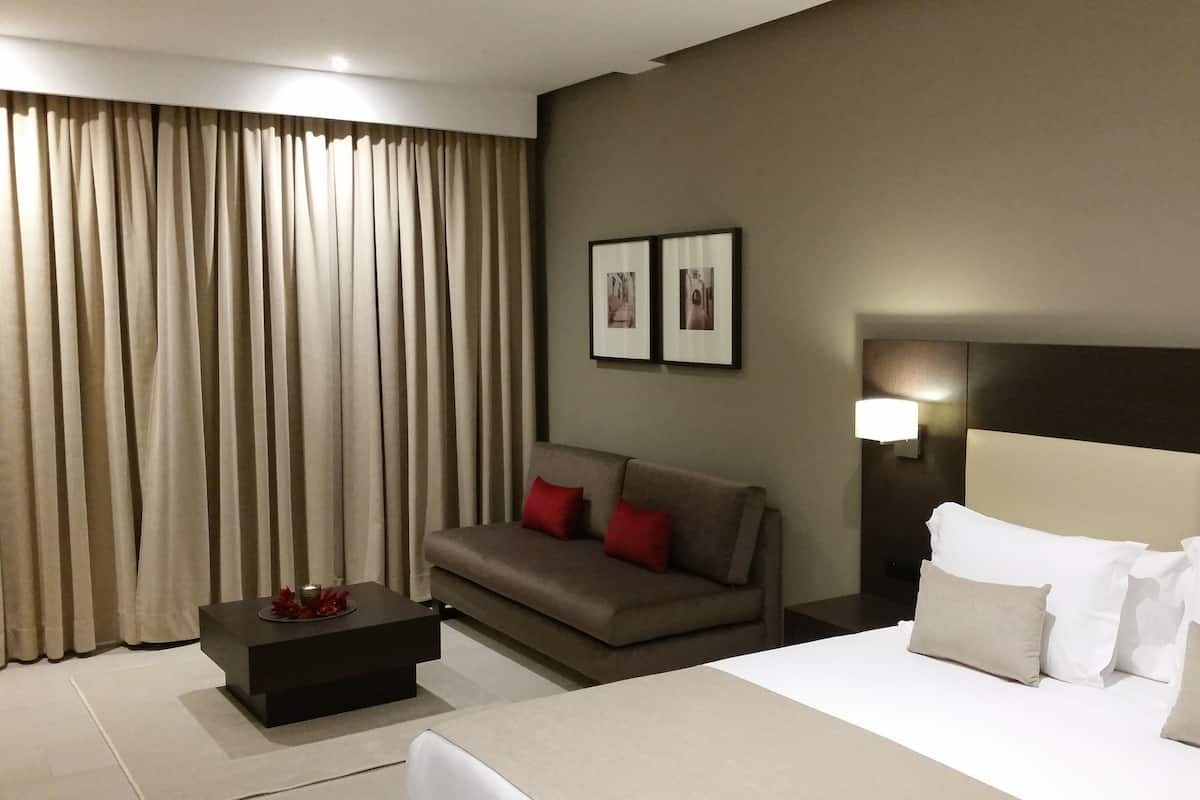 A hotel room with a bed, a sofa, a small table, and a nightstand.